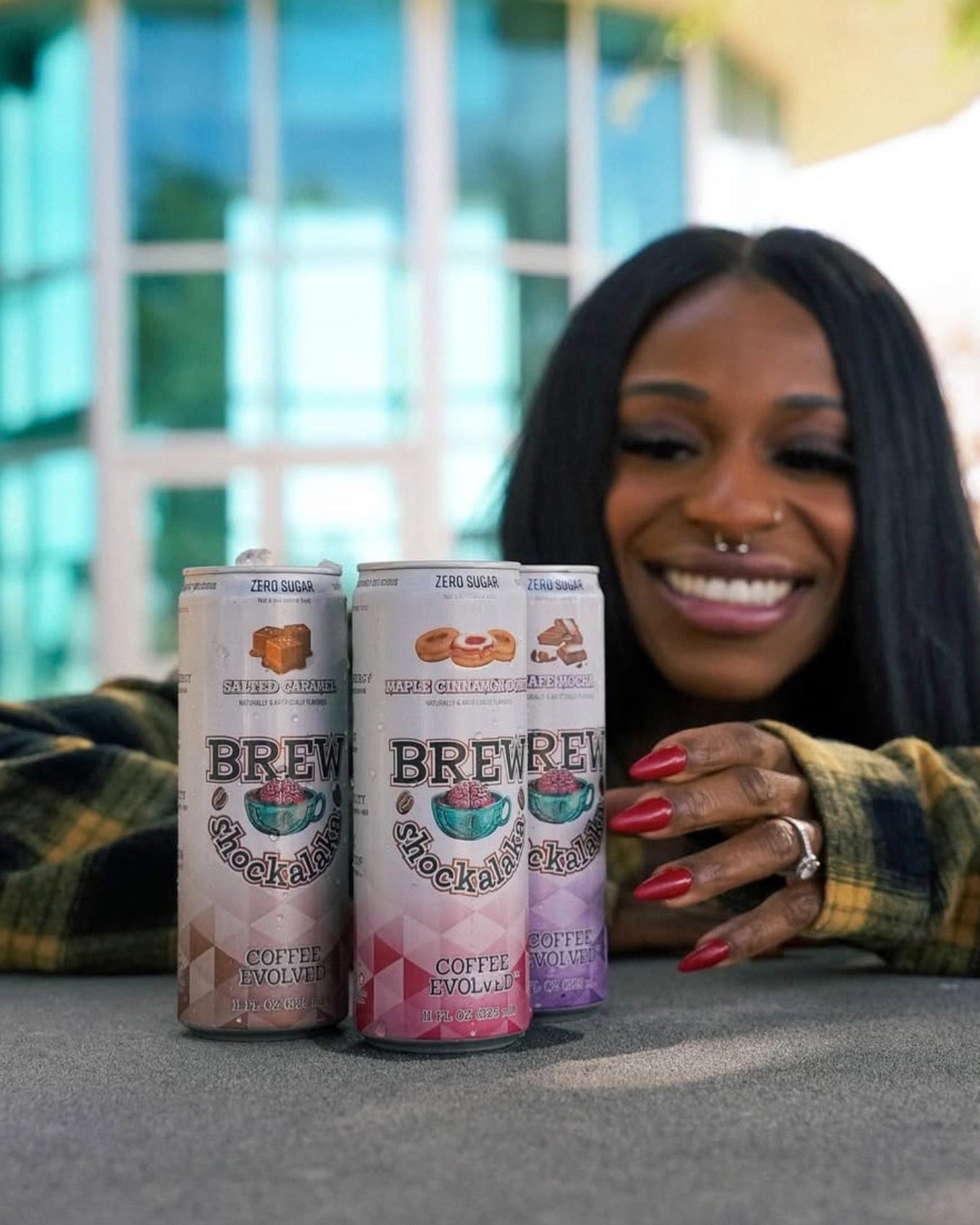 Woman holding three cans of Brewed Coffee Company in front of a blurred outdoor background
