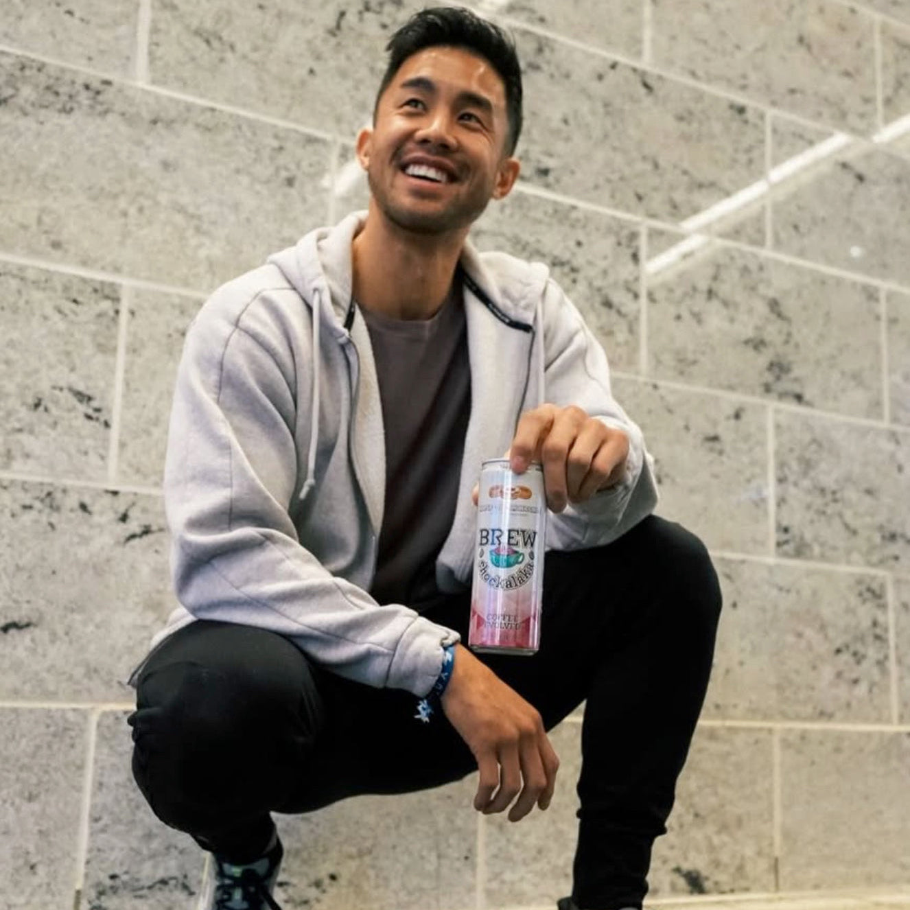 Man holding a can of Brew元気なにわビール against a tiled wall.