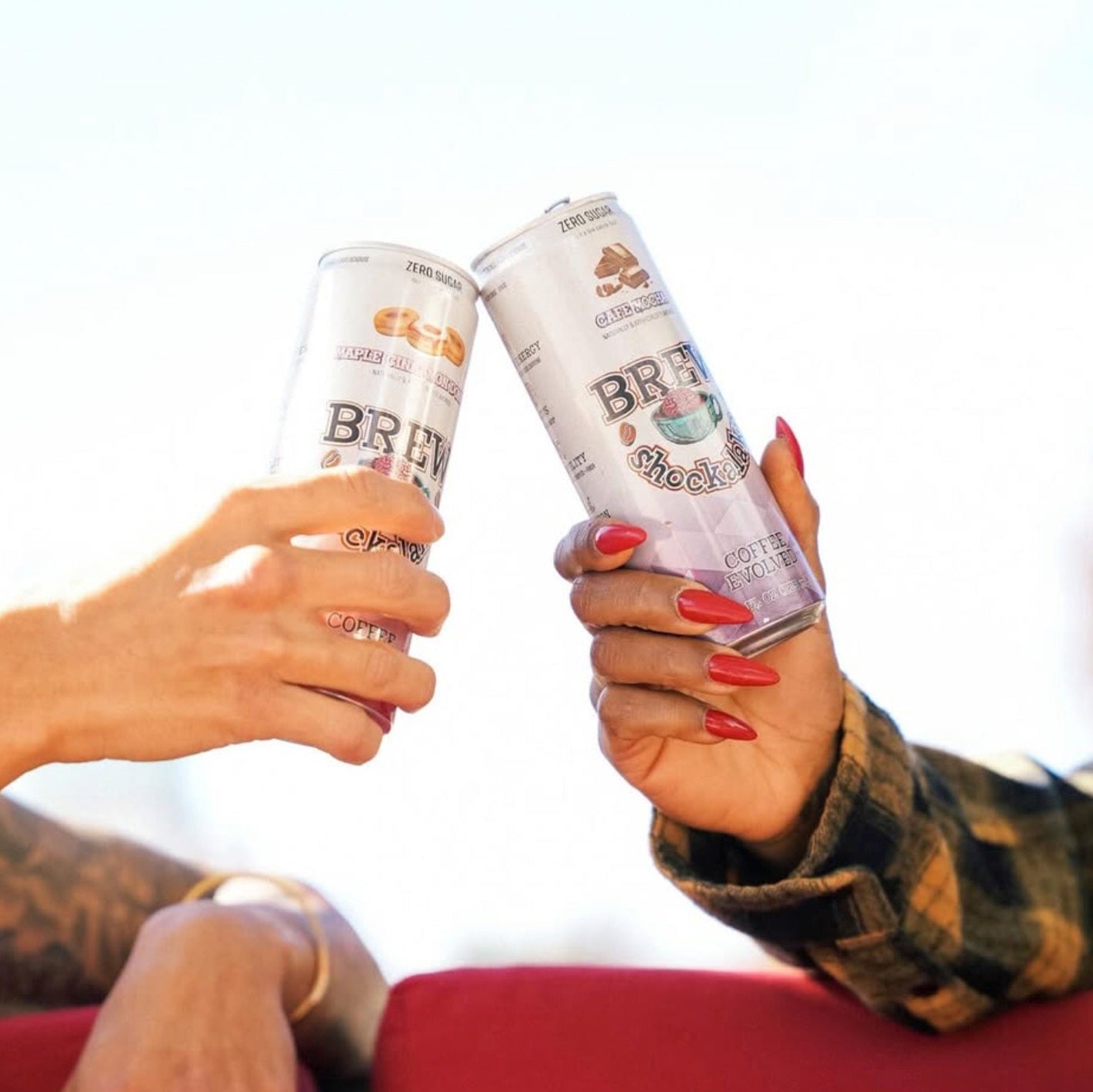 Two hands holding cans of 'Brew' coffee against a blurred background